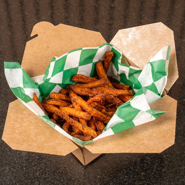 Crispy sweet potato fries in a brown takeout box lined with green and white checkered paper.