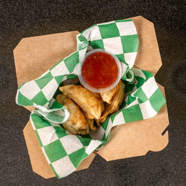 Fried dumplings in a brown paper box lined with green and white checkered paper, with a side of red dipping sauce.