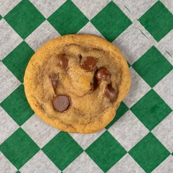 A single chocolate chip cookie rests on green and white checkered wax paper.