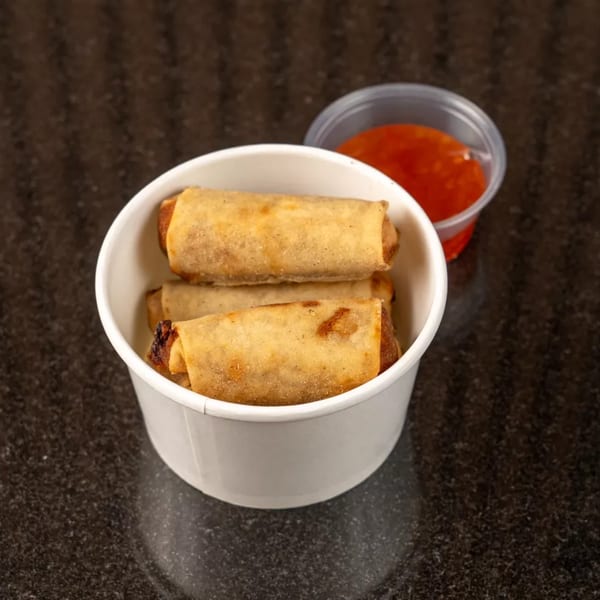 Crispy golden spring rolls in a white container with a side of sweet chili dipping sauce.